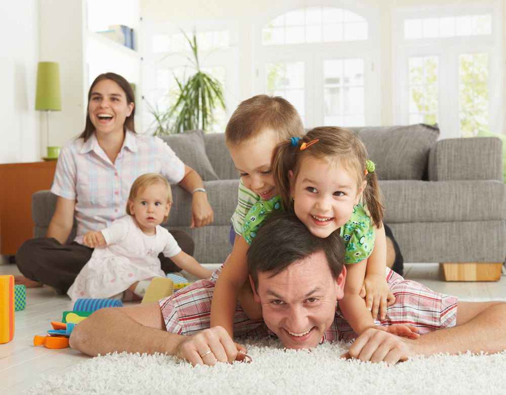 Parents playing with three young children on their living room floor.