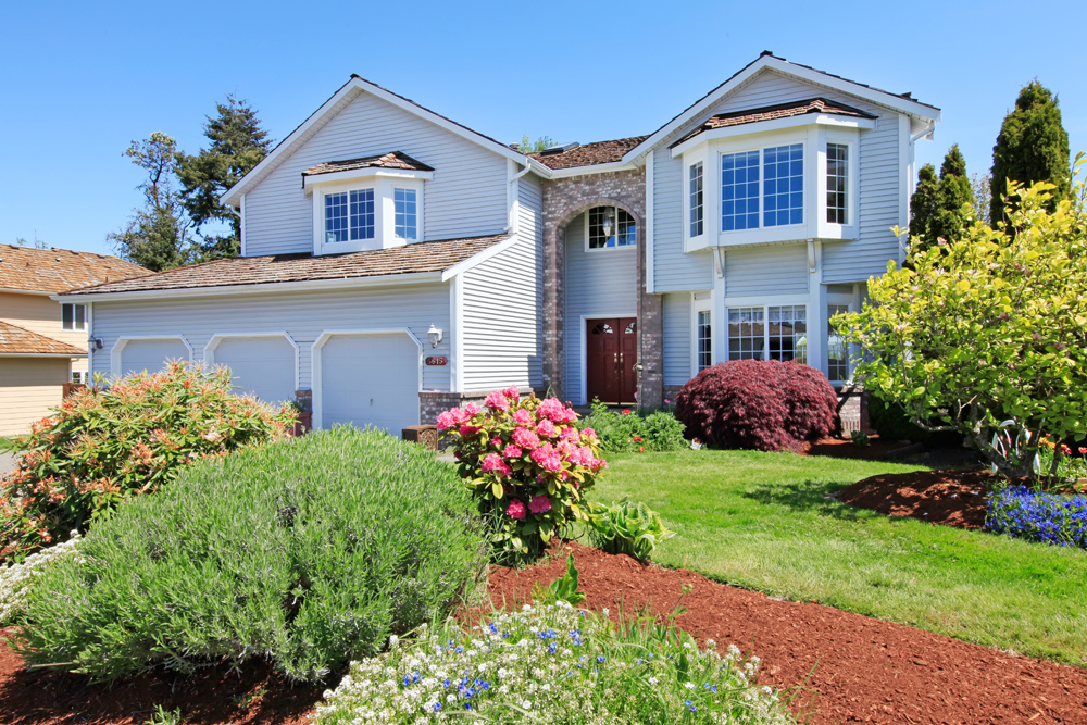 Large two-story house in summer. Landscaped front lawn and three-car garage.
