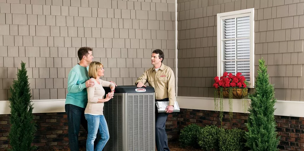Two homeowners standing next to an outdoor AC unit, speaking with an HVAC technician.