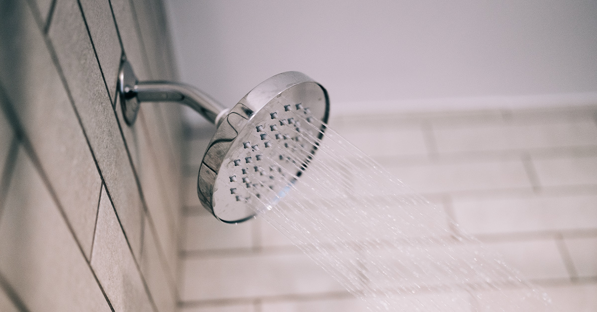 Water coming out of a silver shower head, with white subway tile on walls.